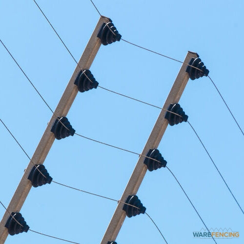 Close up wall mounted high voltage electric security fence instalation isolated against blue sky background